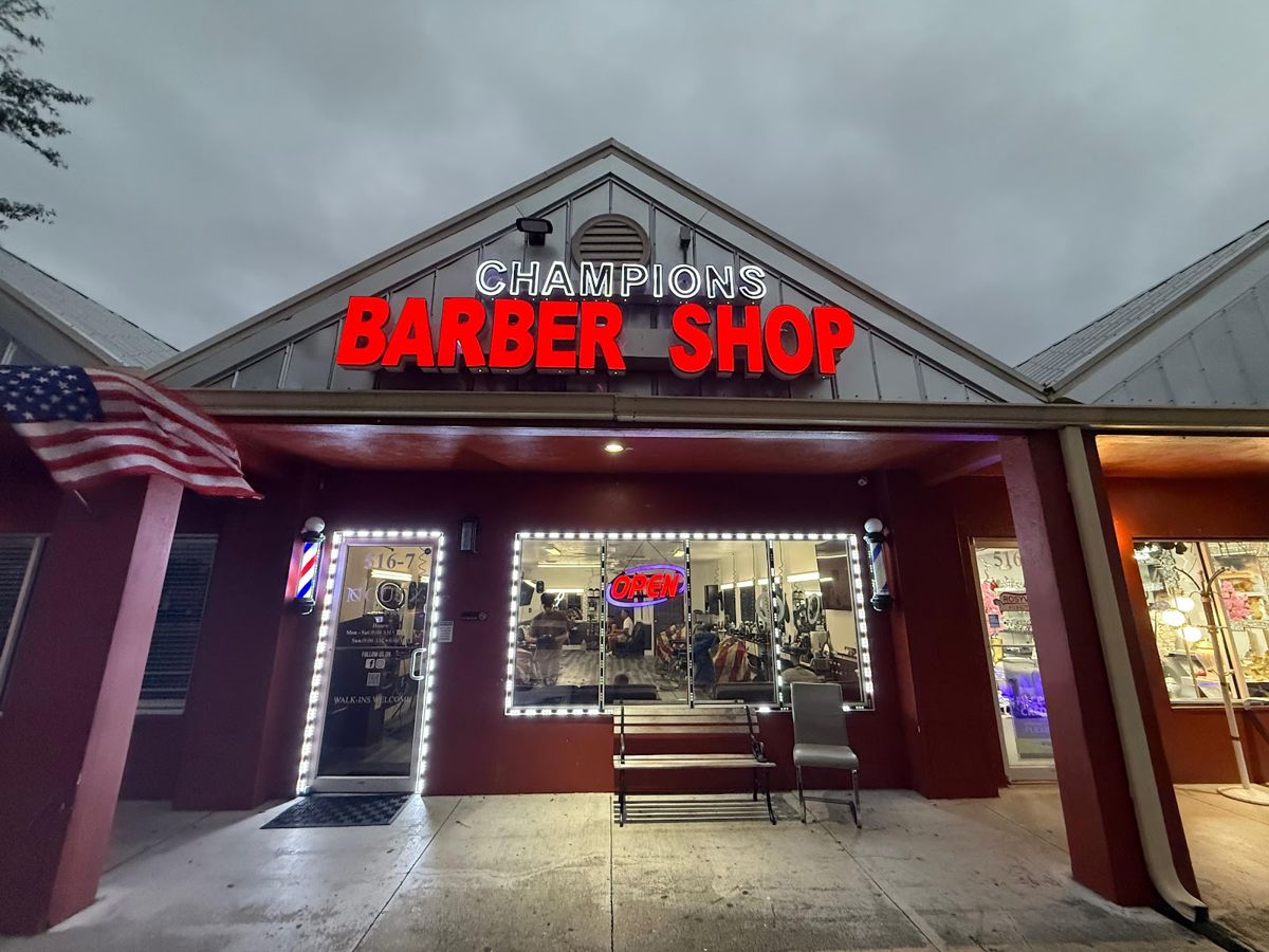 Fachada de Champions Barbershop con letrero rojo "CHAMPIONS BARBER SHOP" y bandera estadounidense